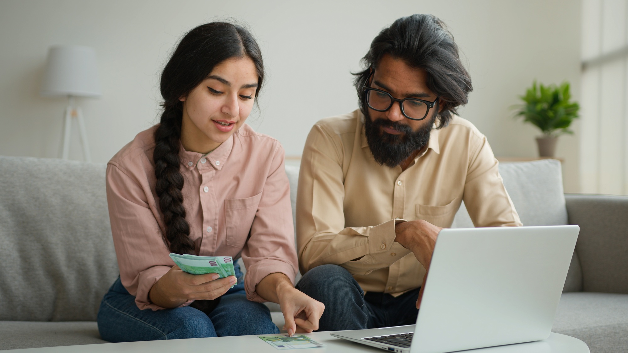 Arabian man Indian woman multiracial couple at home counting euro banknotes salary planning family