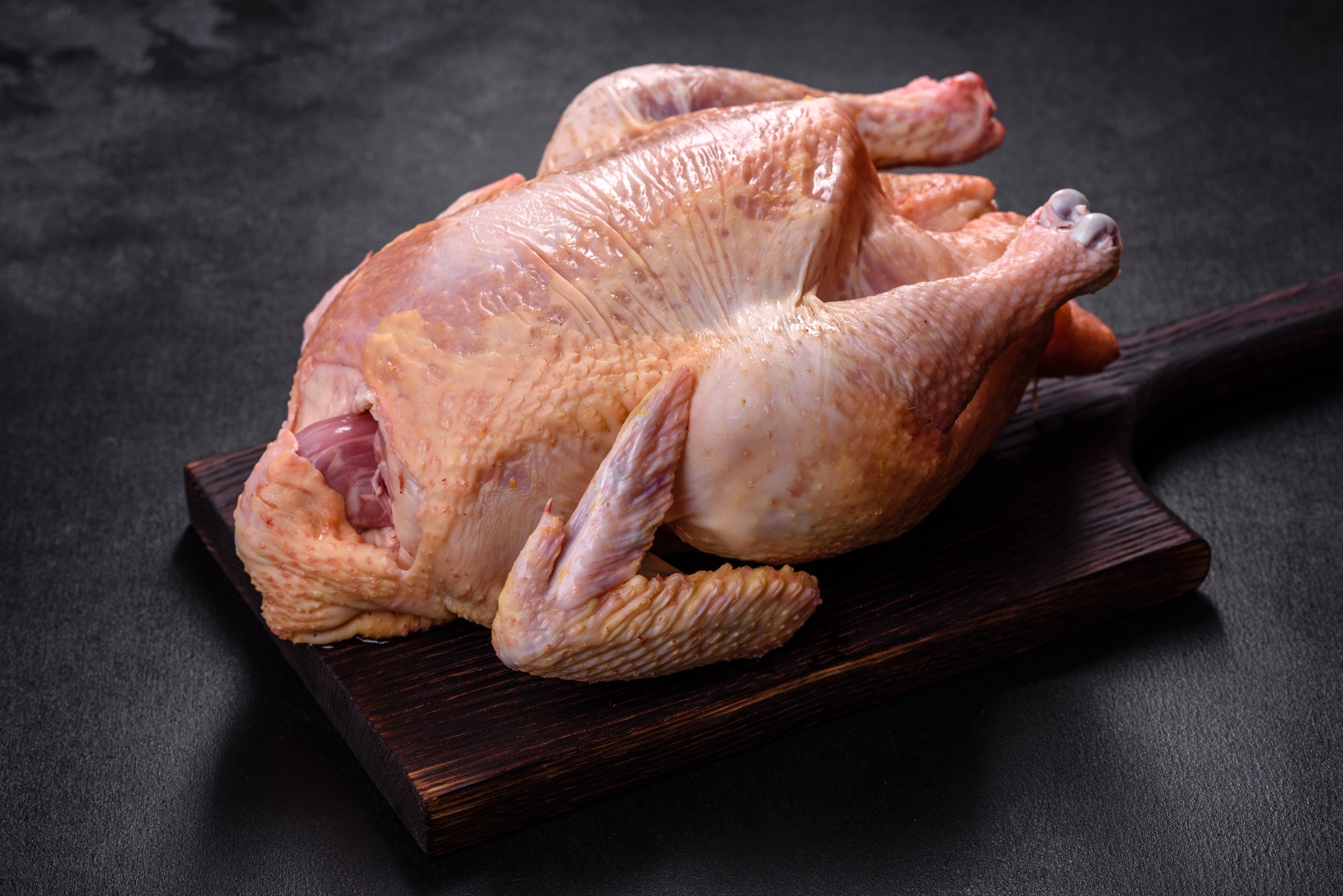 Raw turkey or chicken with salt, spices and herbs on a wooden cutting board